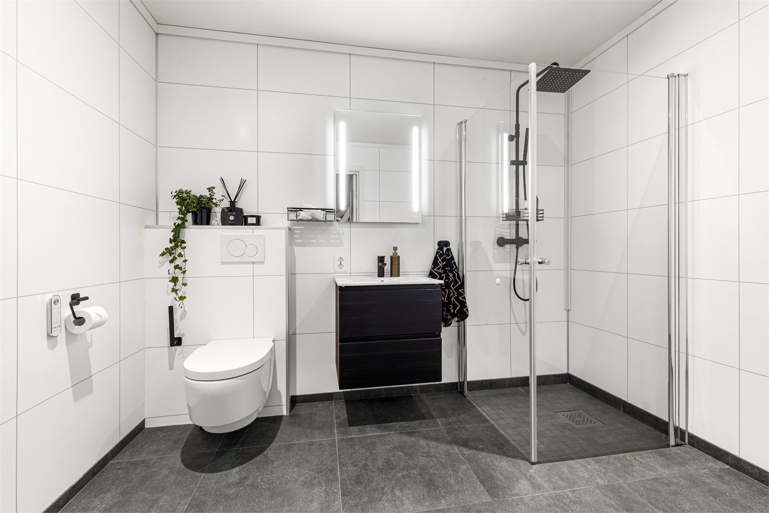 Bad fra byggeår. Flislagt gulv med varme. Baderomsplater på vegger. Himling av malt flate med downlights. Nedsenket dusjsone med innfellbare glassdører. Dusjarmatur tilkoblet hånddusj og regndusj.