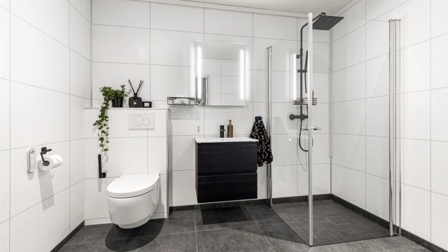 Bad fra byggeår. Flislagt gulv med varme. Baderomsplater på vegger. Himling av malt flate med downlights. Nedsenket dusjsone med innfellbare glassdører. Dusjarmatur tilkoblet hånddusj og regndusj.