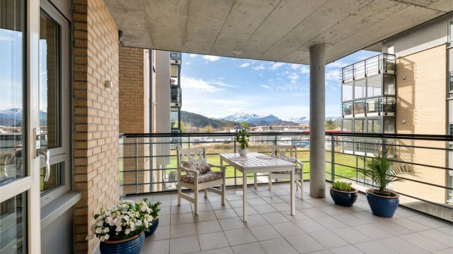 Fra stuen er det utgang til en stor, overbygd terrasse med flislagt gulv og utsikt mot Sunnmørsalpane i sør. Rekkverk i metall og glass.