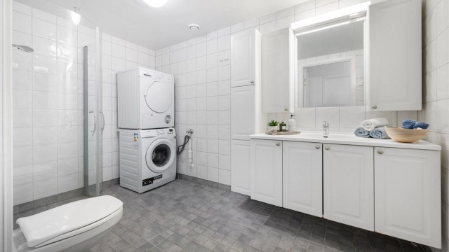 Badet har flislagt gulv med gulvvarme. Flislagte vegger. Takplater i himling. Vegghengt servantinnredning.
