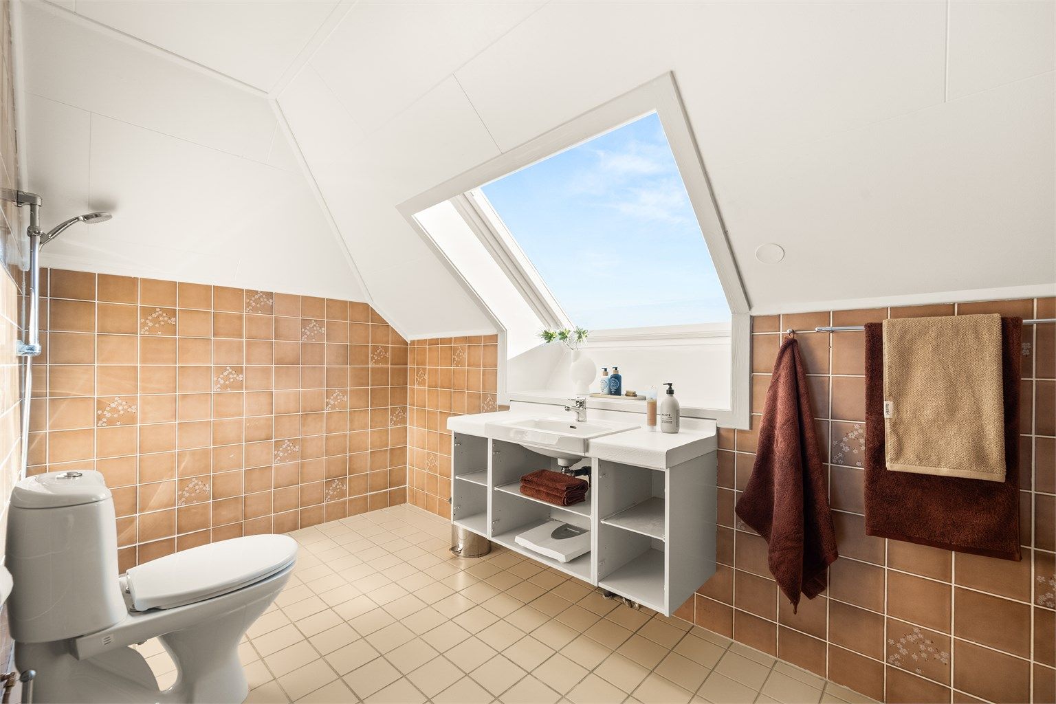 Badet på loftet har flislagt gulv med gulvvarme og et stort takvindu som gir rikelig med dagslys.