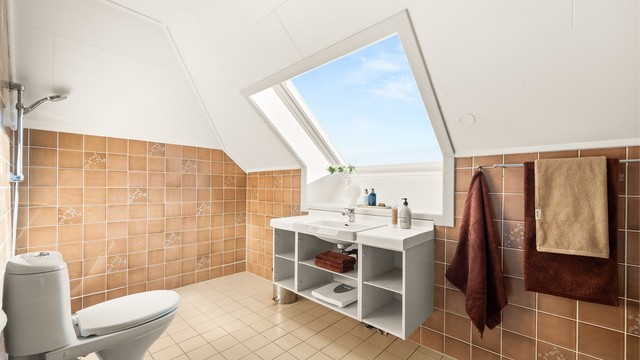 Badet på loftet har flislagt gulv med gulvvarme og et stort takvindu som gir rikelig med dagslys.