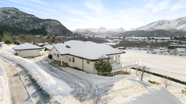 En romslig, asfaltert innkjørsel leder til en dobbelgarasje med installert elbillader.