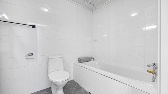 Badet i andre etasje er utstyrt med badekar, flislagt gulv med varmekabler, servantinnredning og gulvstående toalett.