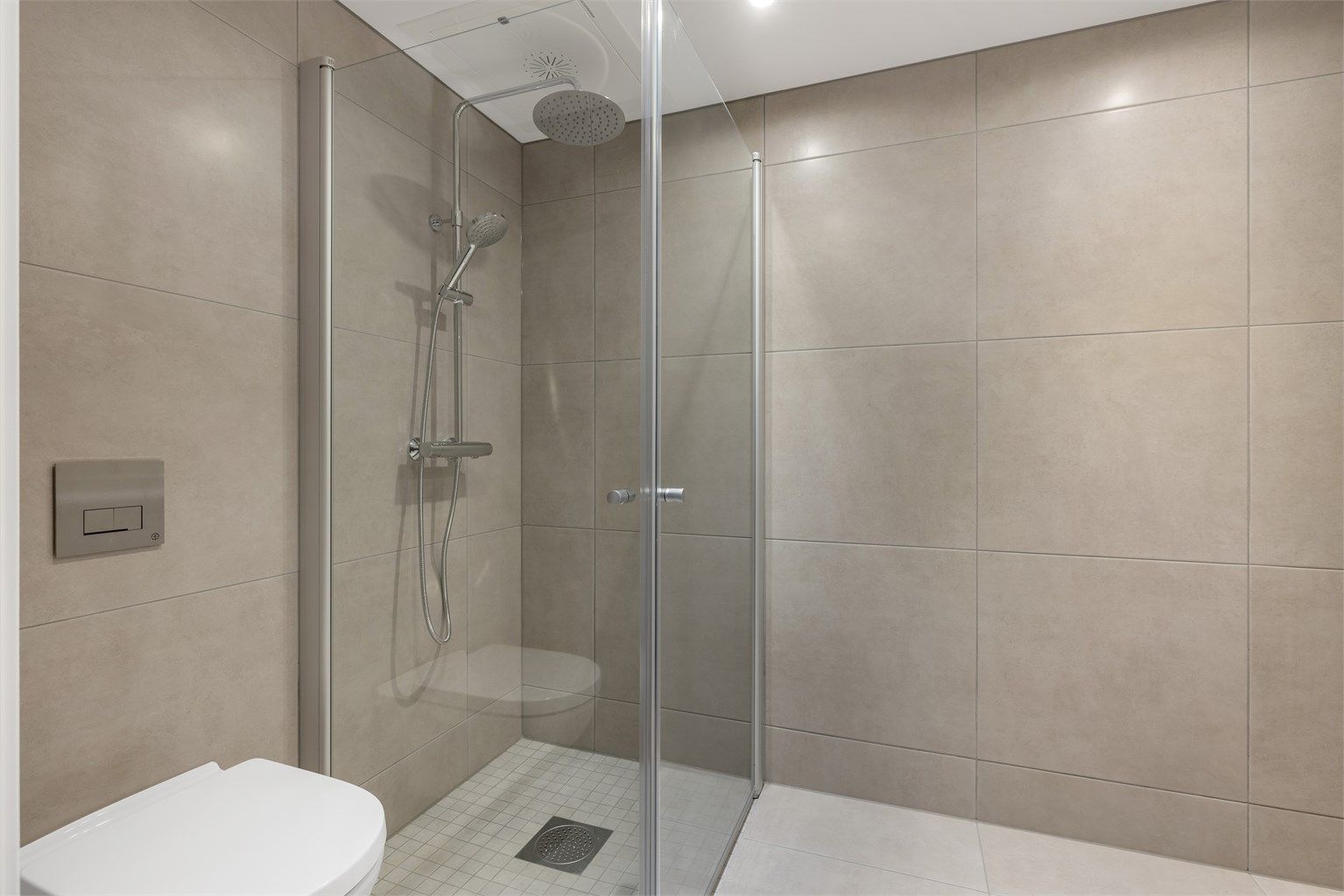 Plass og opplegg til vaskemaskin og tørketrommel. Badet består av veggmontert toalett, dusjdører i herdet glass, veggspeil med integrert belysning, baderomsinnredning med malte fronter og heldekkende servant