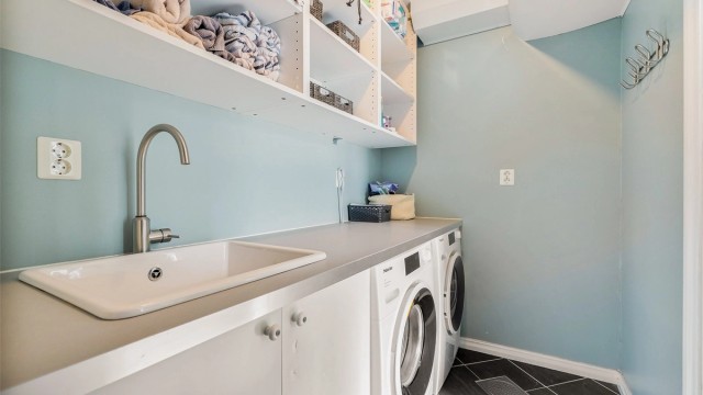 Praktisk vaskeromsdel med opplegg for vaskemaskin og tørketrommel under benkeplate med dør inn fra badet i hovedetasjen.