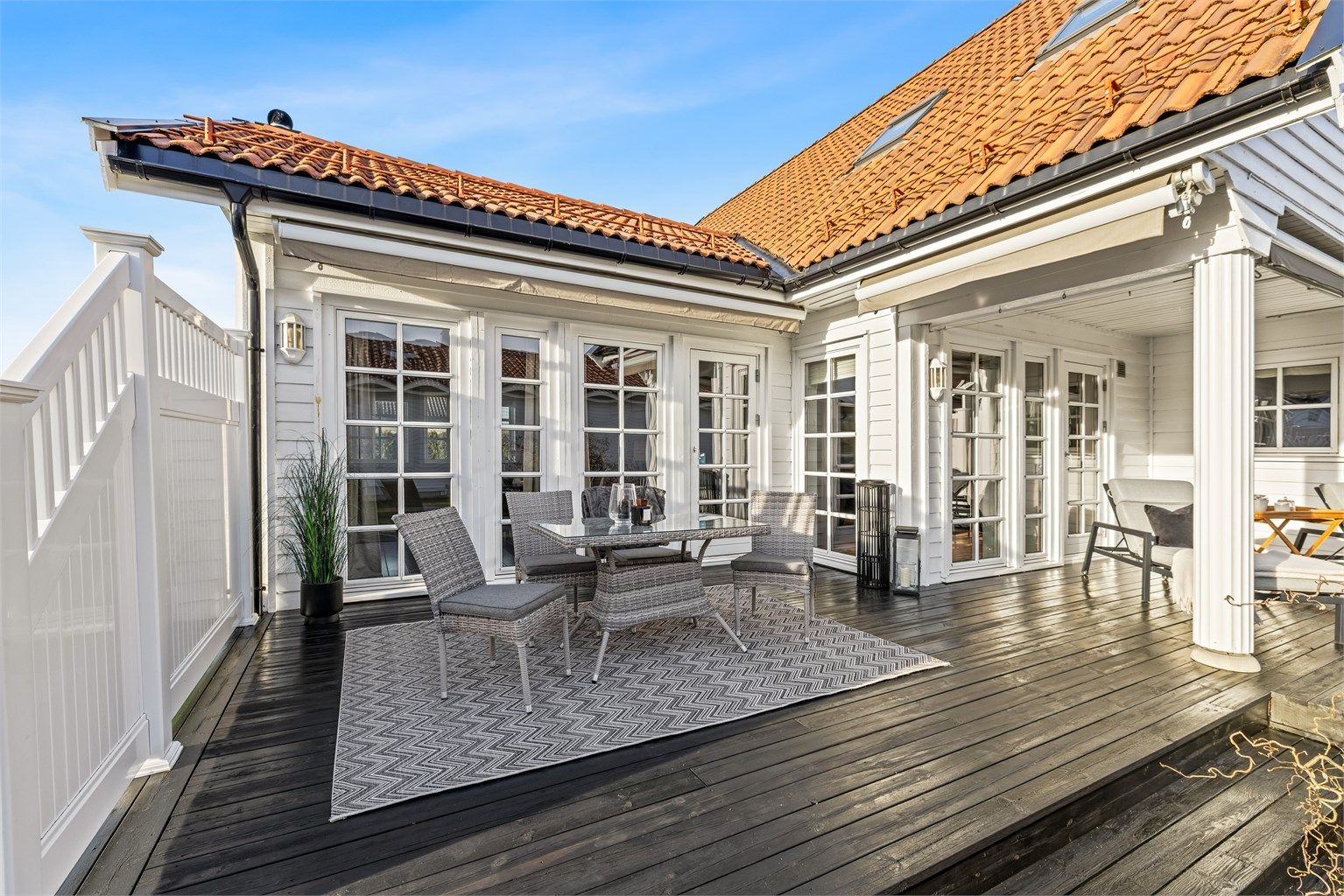 Den L-formede terrassen strekker seg langs to av husets fasader. Delvis overbygget og markisen gir en lun atmosfære. 