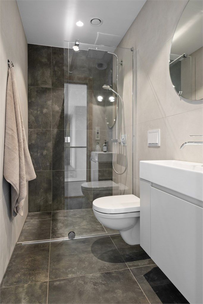 Badet har flislagte gulv og vegger, innredet med servant, vegghengt toalett og dusjhjørne.