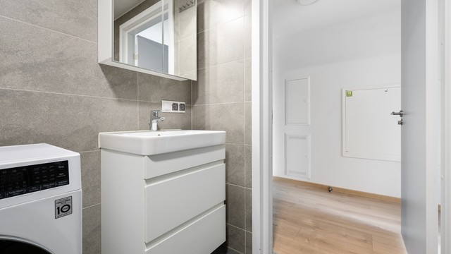 Badet er utstyrt med vegghengt toalett, dusjhjørne med innfellbare dører og servantinnredning med speilskap.