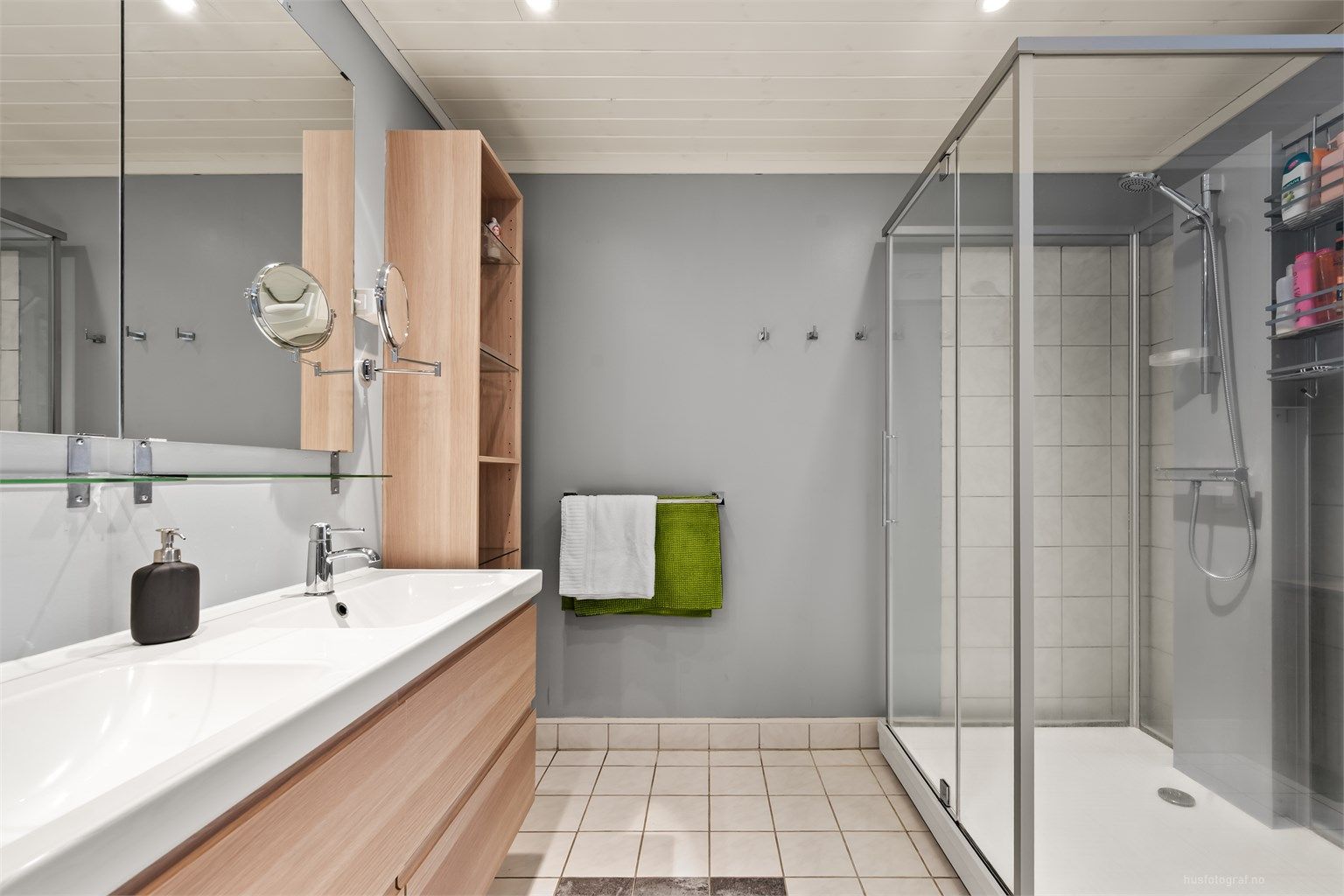 Fliser på gulv med gulvvarme, flislagte vegger i dusjsonen, malte tapetserte veggflater og panelbord i himling med downlights 