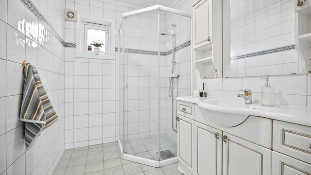 Bad i 1. etasje med flislagte overflater, gulvvarme og dusjhjørne.