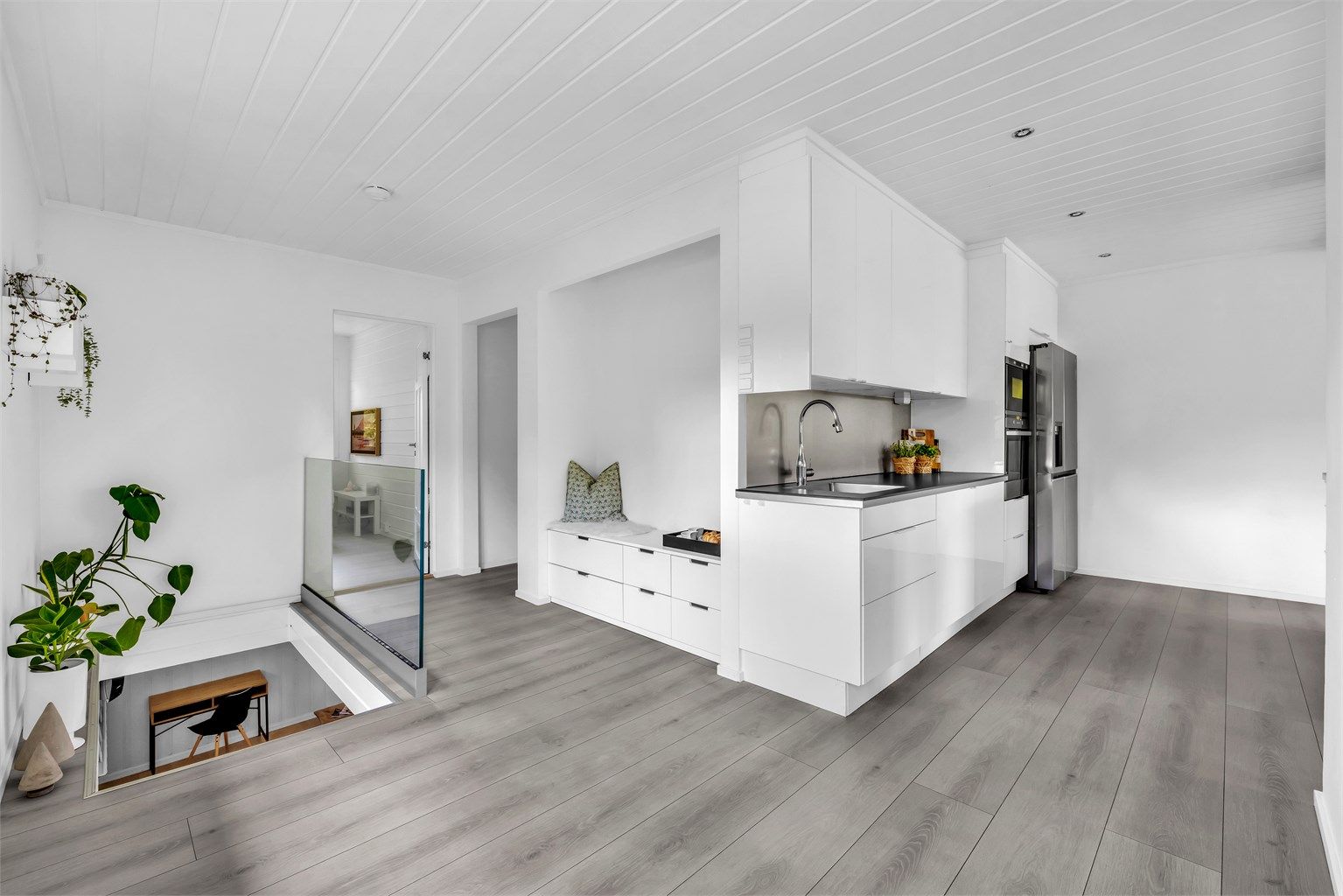 Kjøkkenet er utstyrt med integrerte hvitevarer som oppvaskmaskin, komfyr og mikrobølgeovn plassert i høyskap, samt et frittstående kjøleskap, noe som bidrar til et sømløst design. 