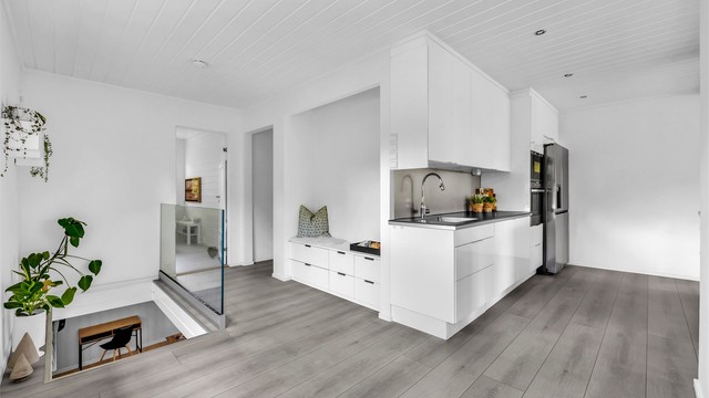 Kjøkkenet er utstyrt med integrerte hvitevarer som oppvaskmaskin, komfyr og mikrobølgeovn plassert i høyskap, samt et frittstående kjøleskap, noe som bidrar til et sømløst design.
