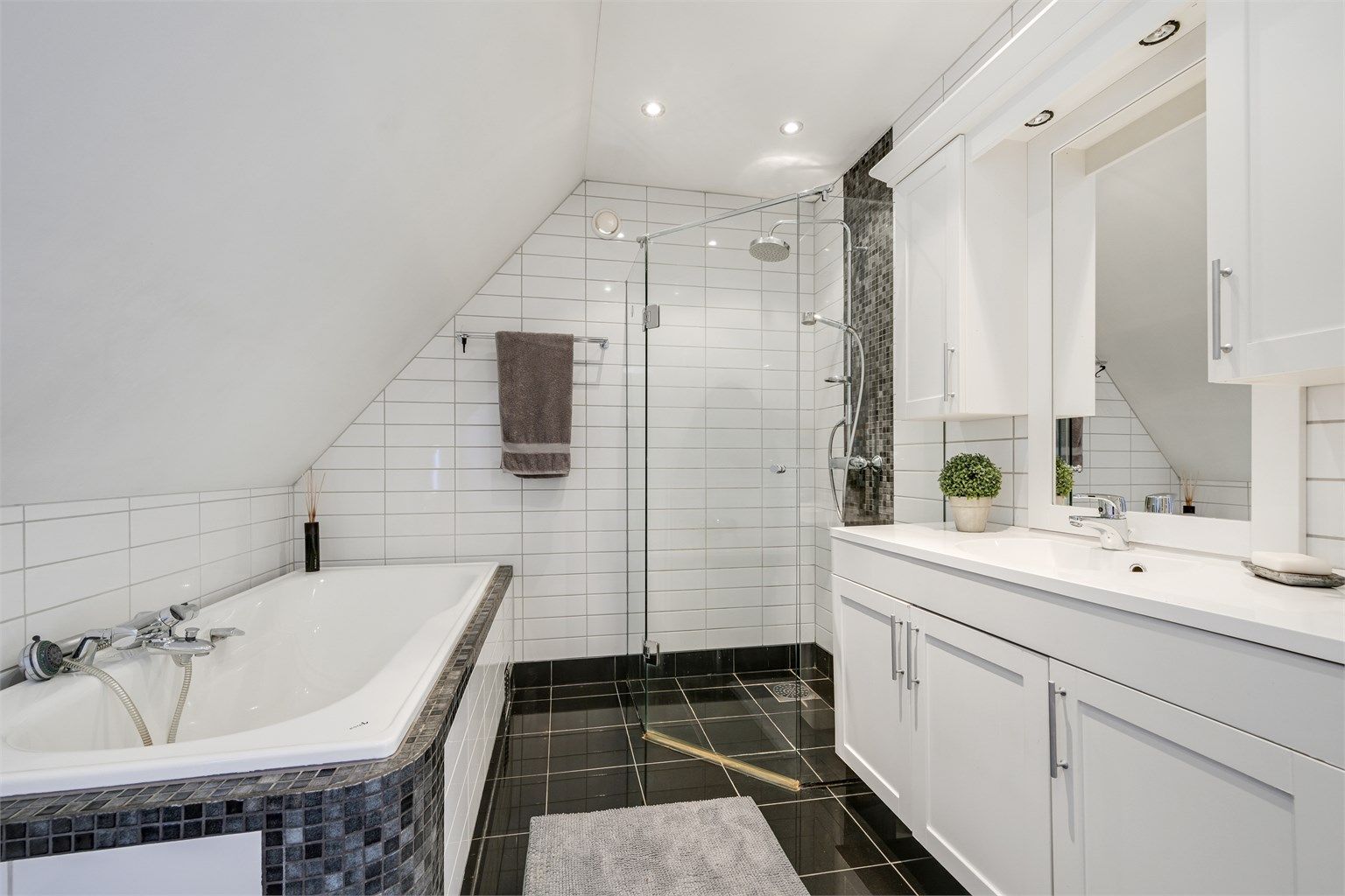 Badet er innredet med servant med underskap, innfliset badekar, dusjvegger og vegghengt toalett.