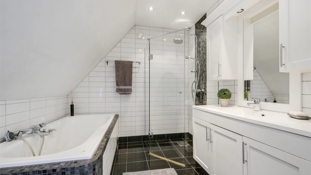 Badet er innredet med servant med underskap, innfliset badekar, dusjvegger og vegghengt toalett.