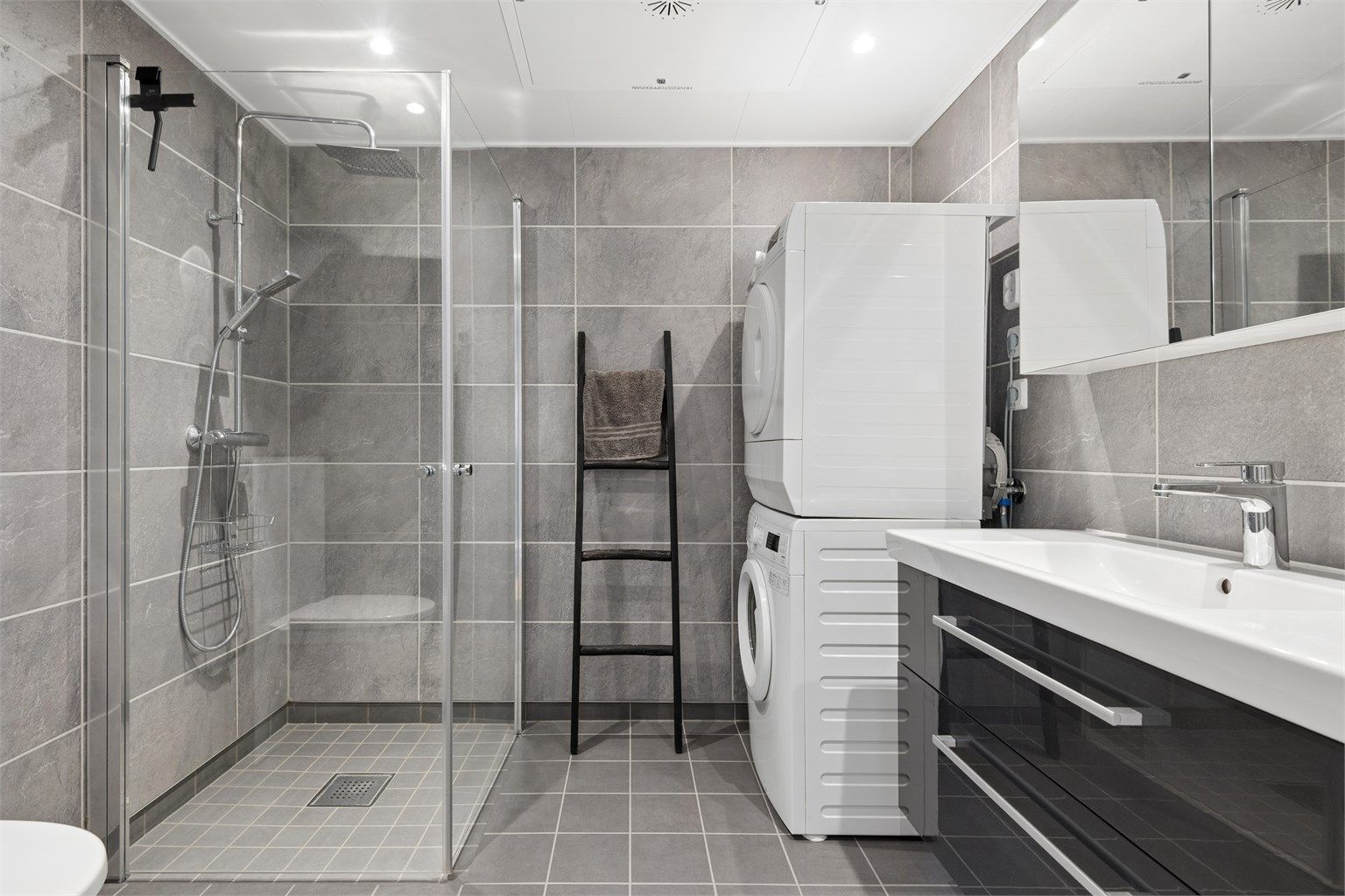 Badet har flislagte gulv og vegger, samt gulvvarme. Det er innredet med servant, speilskap, dusjhjørne med både hånddusj og regndusj, vegghengt toalett og opplegg for vaskemaskin.