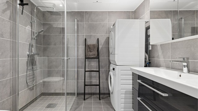 Badet har flislagte gulv og vegger, samt gulvvarme. Det er innredet med servant, speilskap, dusjhjørne med både hånddusj og regndusj, vegghengt toalett og opplegg for vaskemaskin.