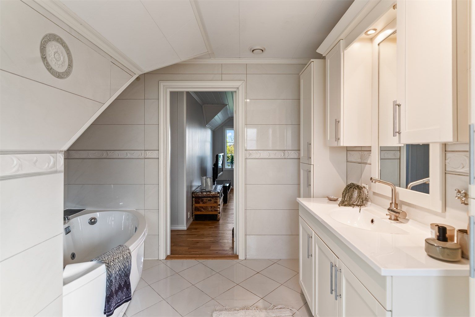 Det er montert vegghengte skap og baderomsinnredning med heldekkende servant. Speil, skap, overlys og stikkontakt er montert på vegg over servanten. Badekar og vegghengt toalett.