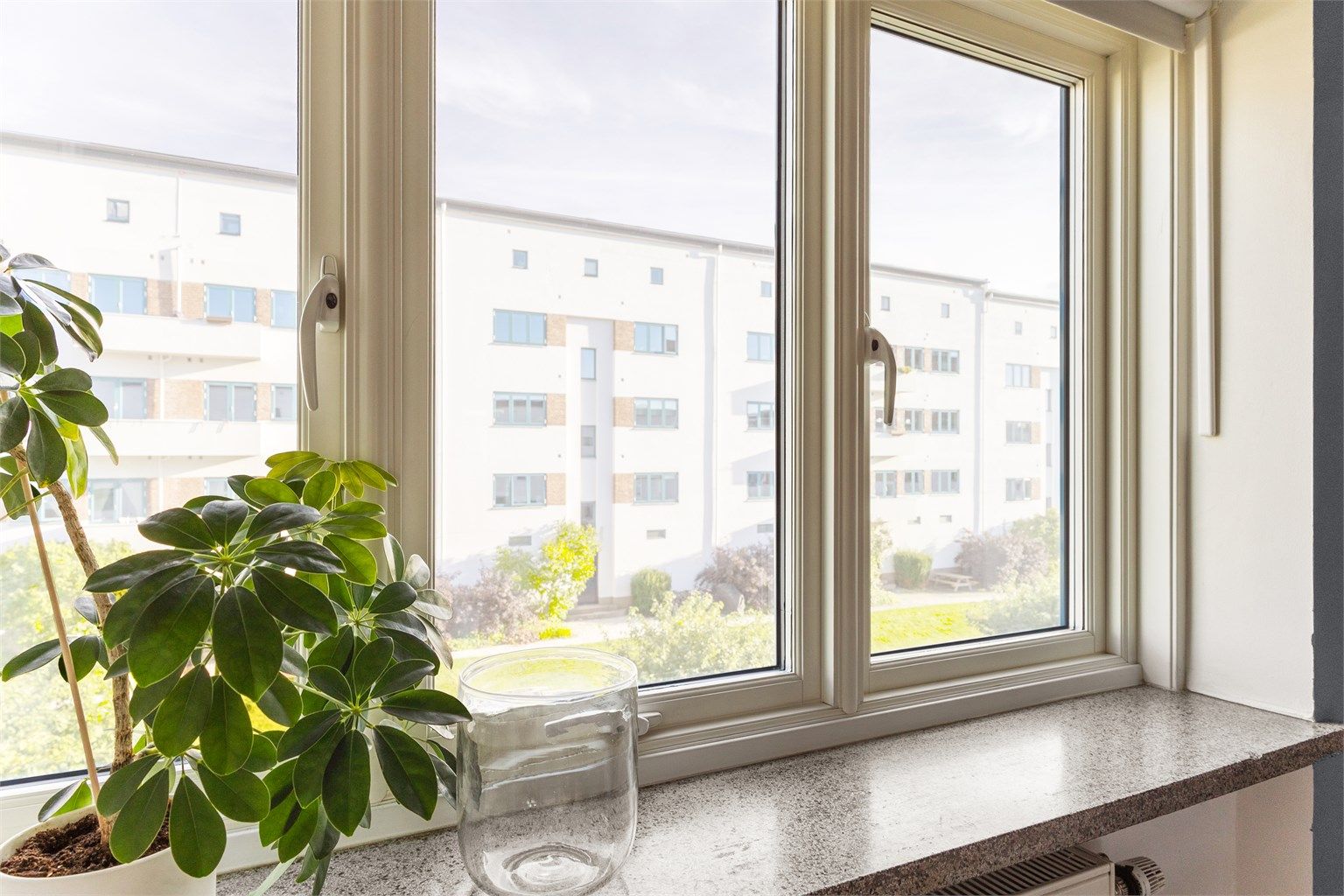 Dype vinduskarmer gir plass til grønne planter og ekte bygårdssjarm. Herfra ser du ned på Funkisgårdens skjermede og gartnerstelte bakgård, som blomstrer gjennom hele sesongen og er et populært samlingspunkt for naboene.