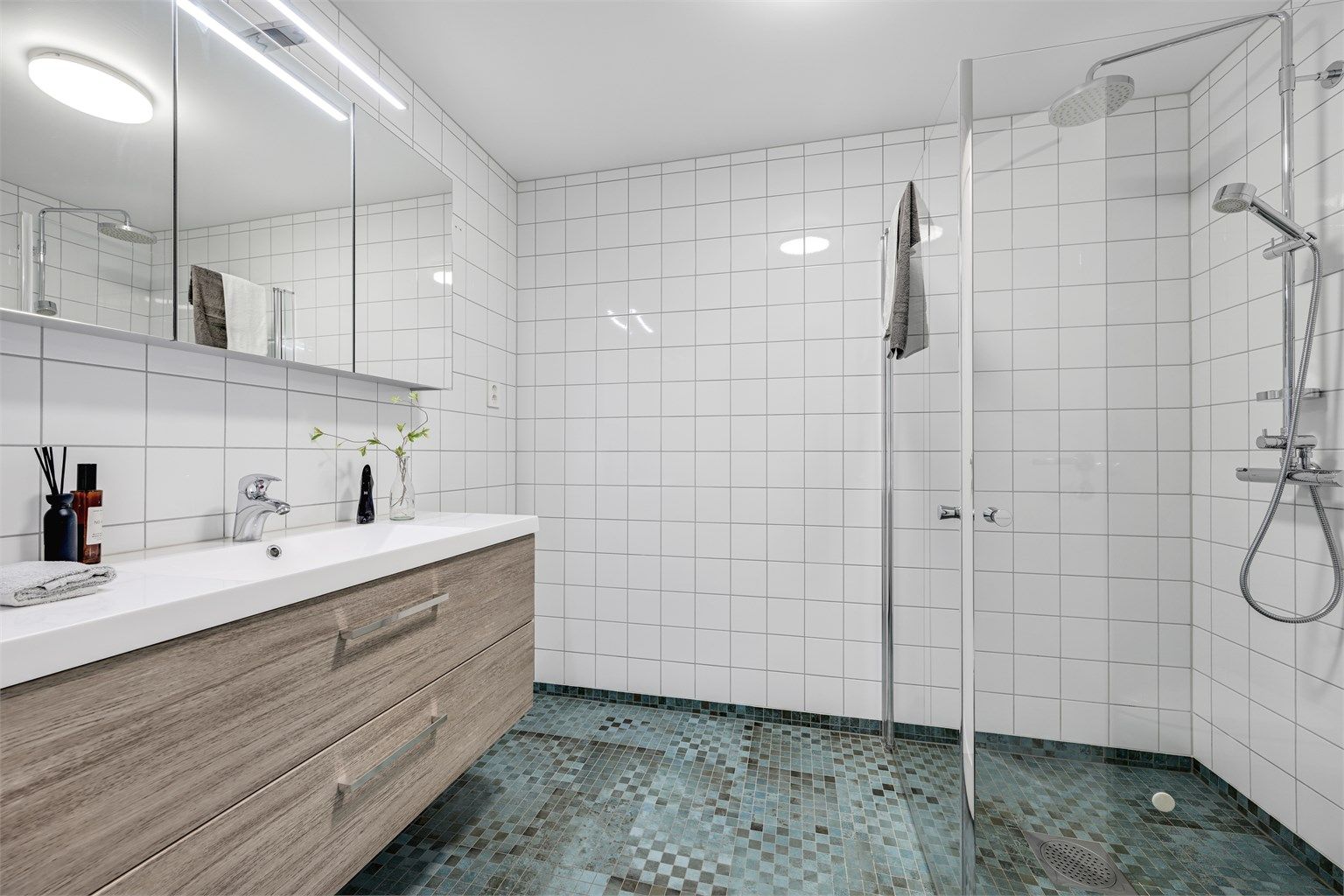 Badet i første etasje har fliser på gulv og vegger, gulvvarme og dusjhjørne med glassvegger.