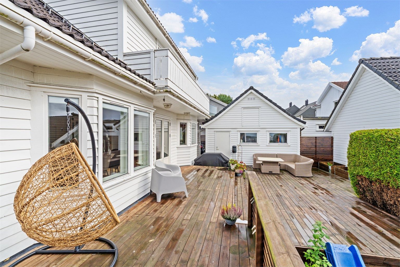 Terrassen er belagt med terrassebord og omkranset av tett hekk.