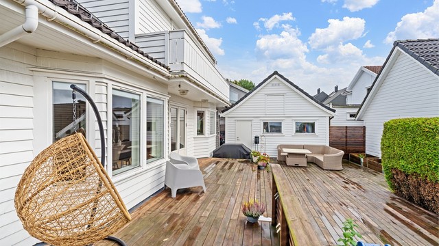 Terrassen er belagt med terrassebord og omkranset av tett hekk.