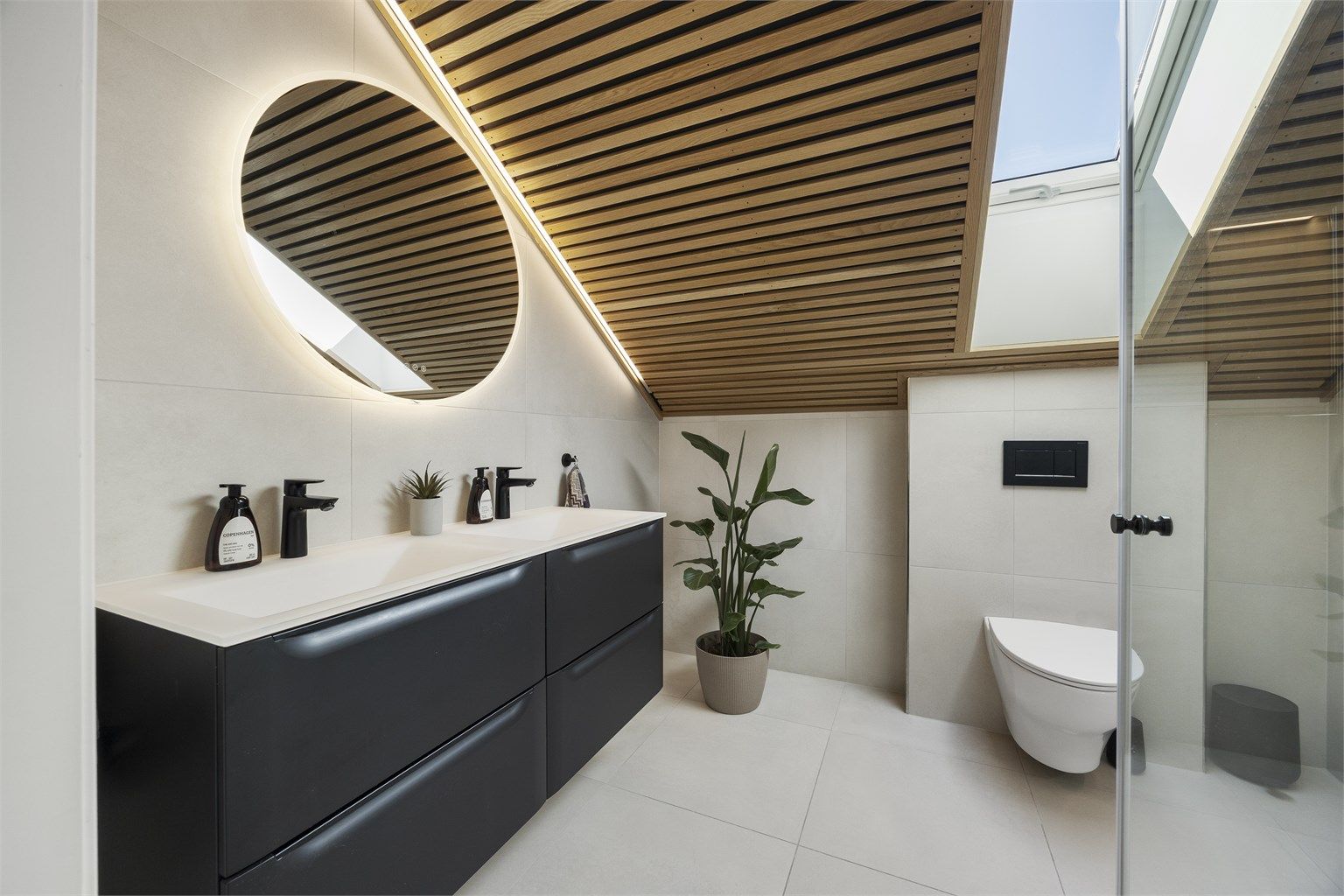 Innredningen har dobbel, ovenpåliggende servant og sorte armaturer som understreker den moderne stilen.