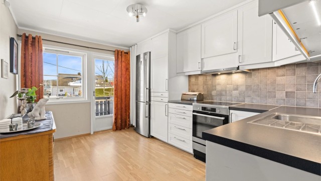 Romslig kjøkken med god benkeplass. Fliser på vegg mellom kjøkkenbenk og overskap.