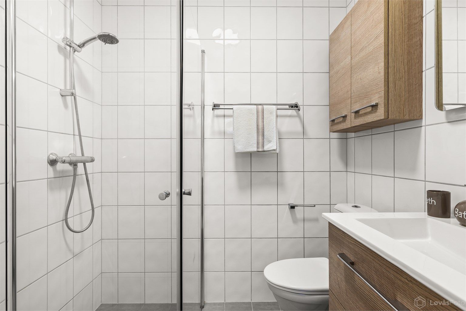 Badet har dusj med glassvegger og opplegg for vaskemaskin.
