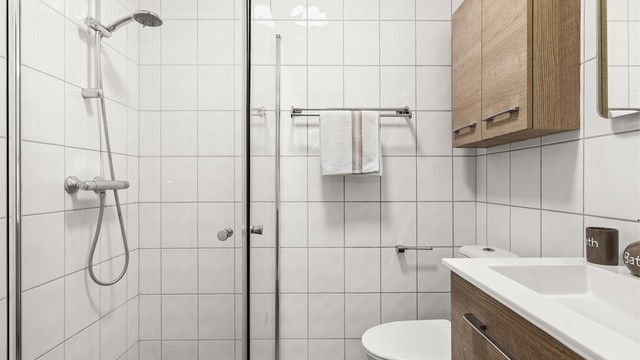 Badet har dusj med glassvegger og opplegg for vaskemaskin.