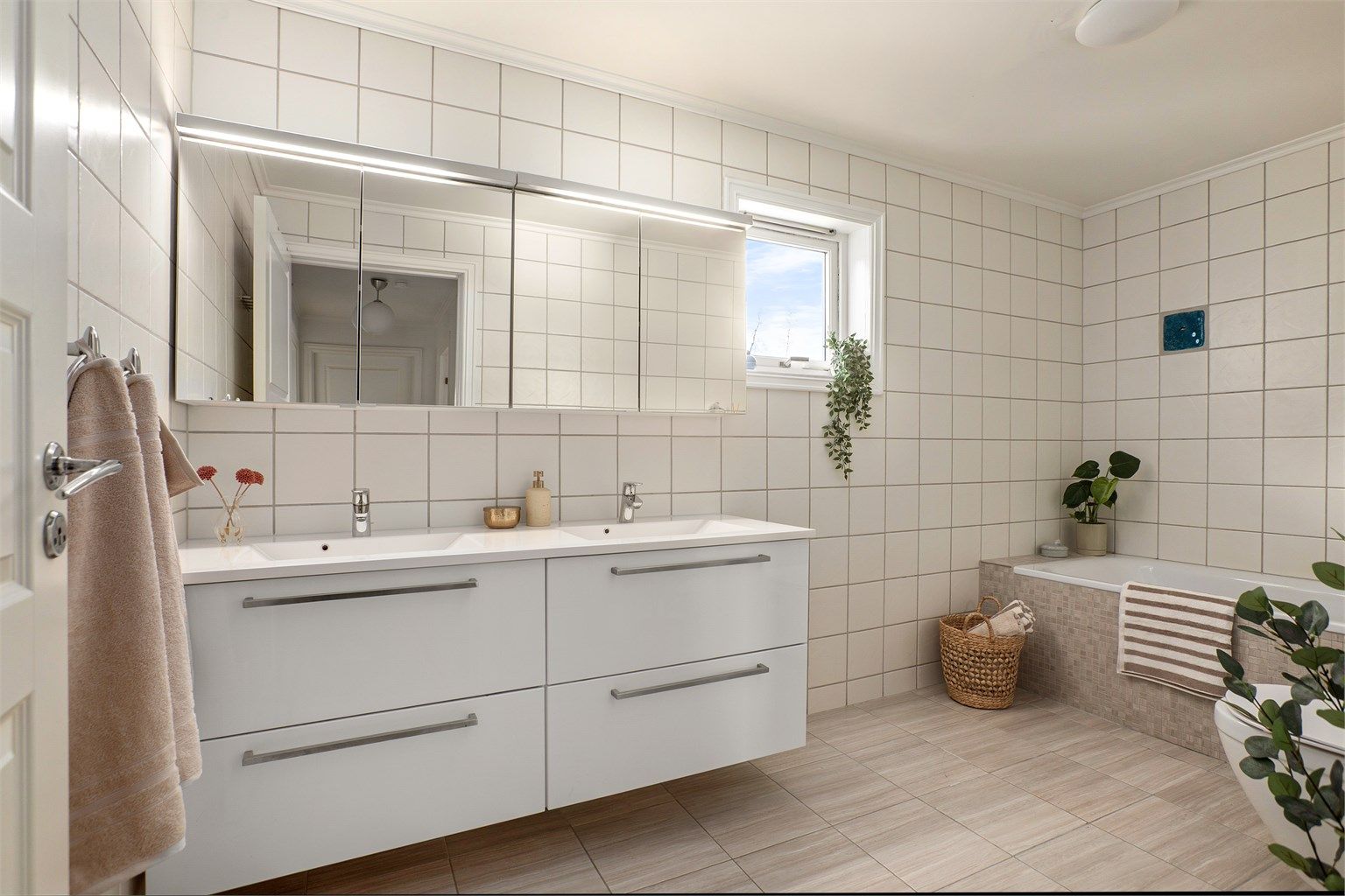 Badet er innredet med servantinnredning med dobbel servant, speilskap med belysning, badekar med vegghengt armatur og vegghengt toalett