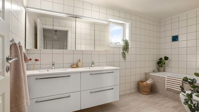 Badet er innredet med servantinnredning med dobbel servant, speilskap med belysning, badekar med vegghengt armatur og vegghengt toalett