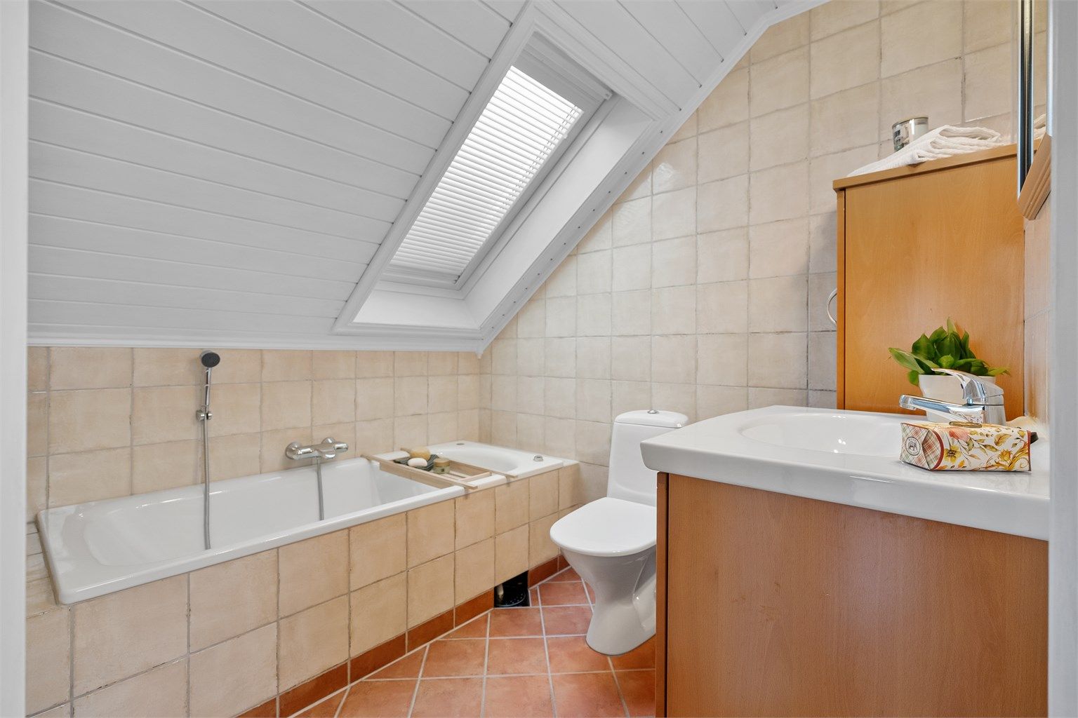 Badet på loftet har flislagt gulv med gulvvarme og et innmurt badekar.