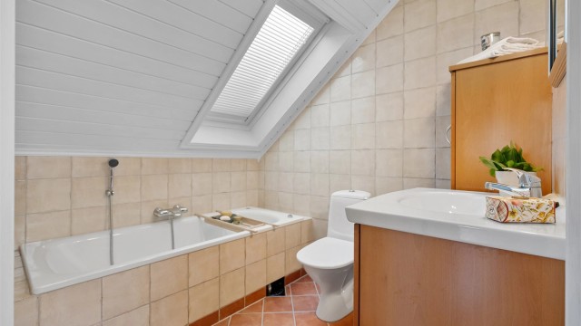 Badet på loftet har flislagt gulv med gulvvarme og et innmurt badekar.
