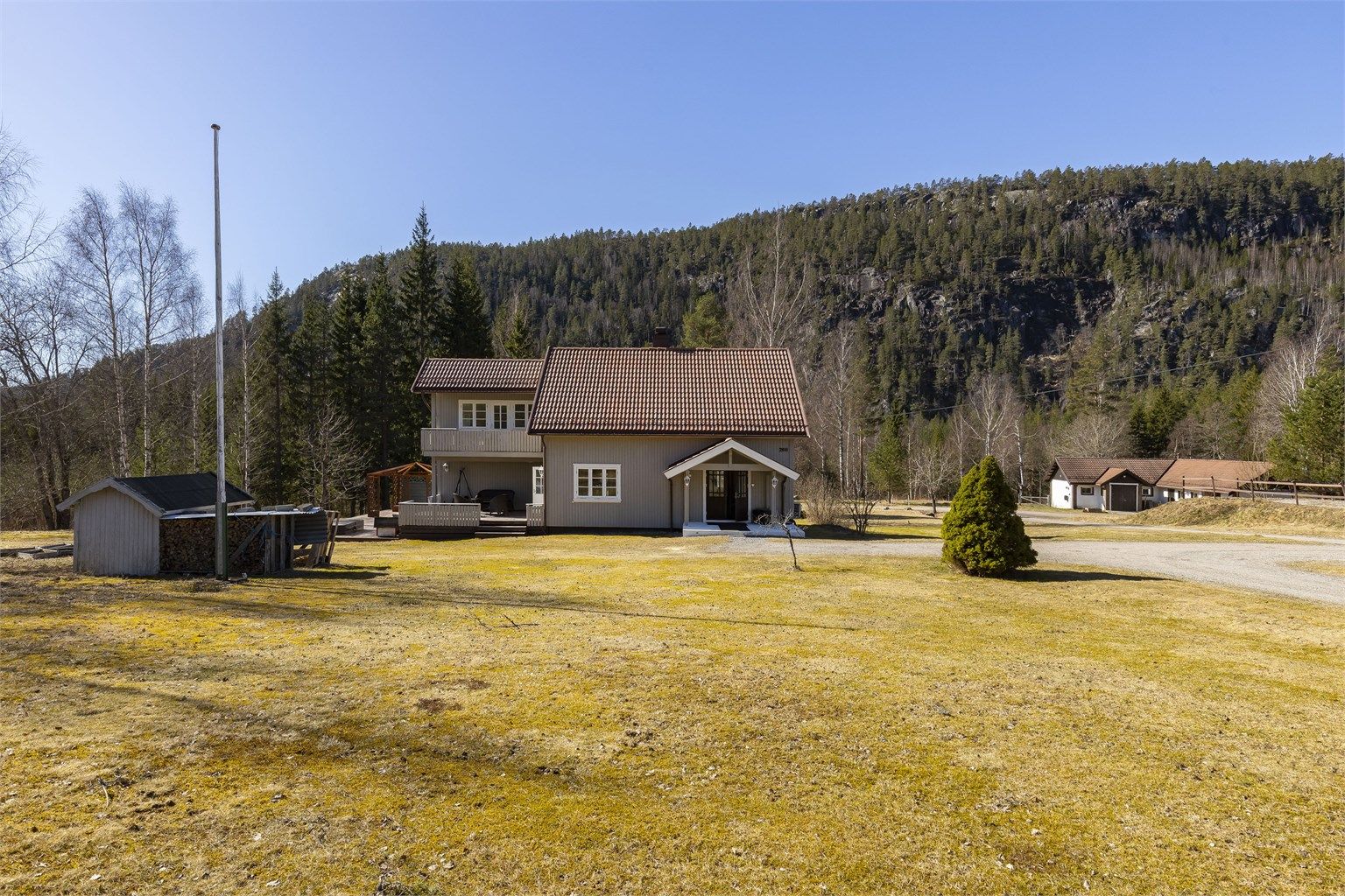 Oversiktsbilde av eiendommen med tilhørende bod til venstre og stall/verksted til høyre.