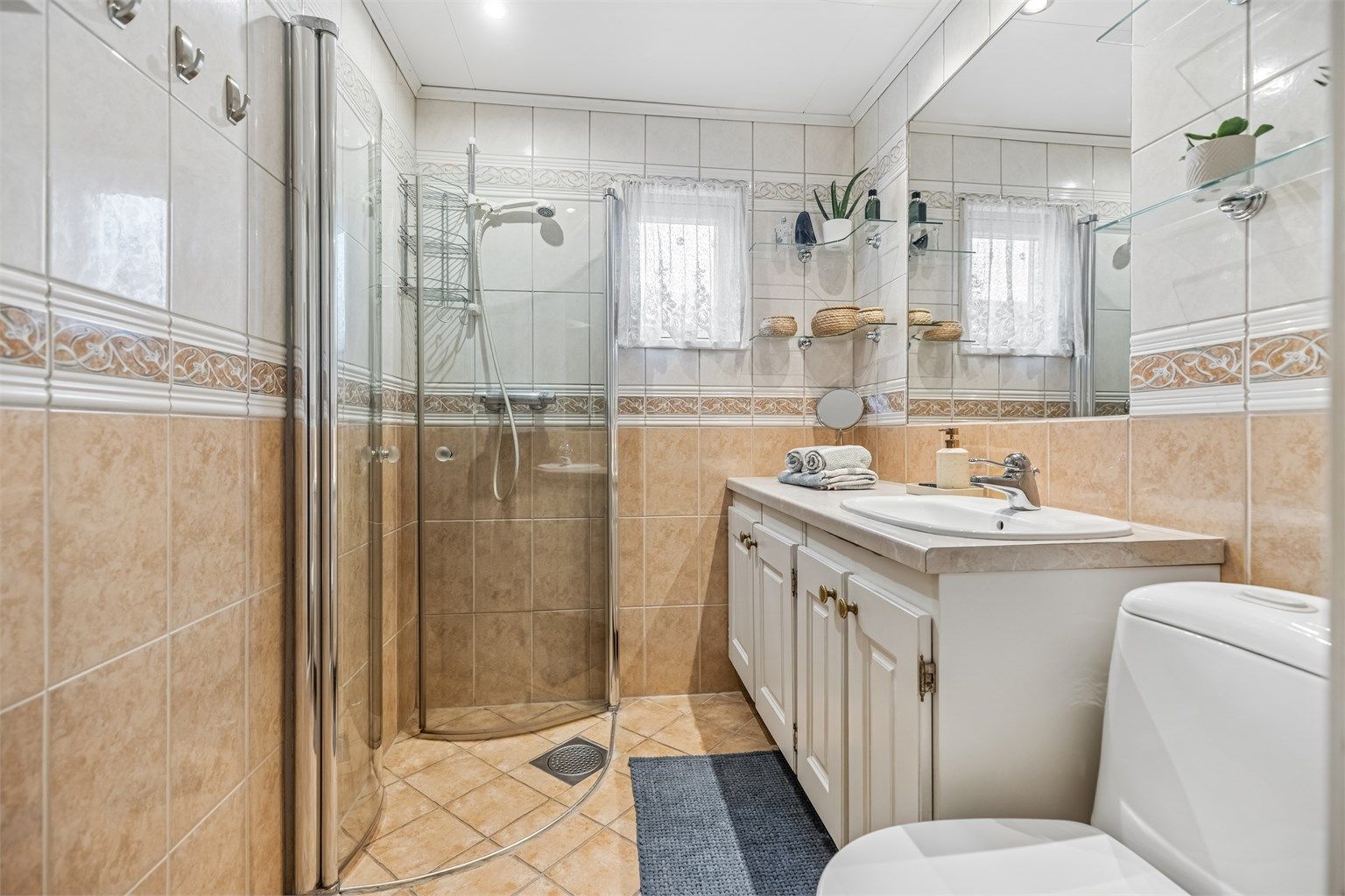 Flislagt bad med gulvvarme. Stor servantinnredning med god plass til oppbevaring. Dusjhjørne med innadslående glassdører samt gulvstående toalett.