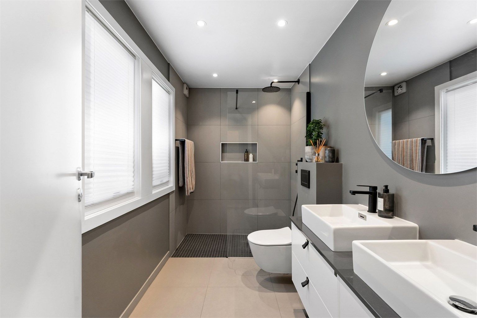 Lekkert bad fra 2018 med fliser på gulv og på vegger. Badet har servantinnredning med doble vasker, vegghengt toalett og dusj med glassvegg. Det er malt himling med downlights