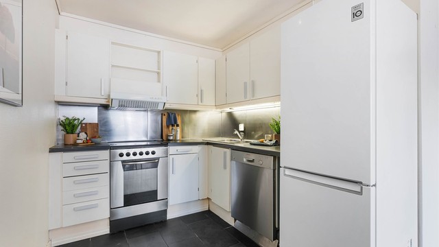 Kjøkkeninnredning med profilerte fronter og benkeplate med laminert overflate. Frittstående komfyr, oppvaskmaskin og kjøleskap med fryser. Ventilator i overskap fungerer ikke.