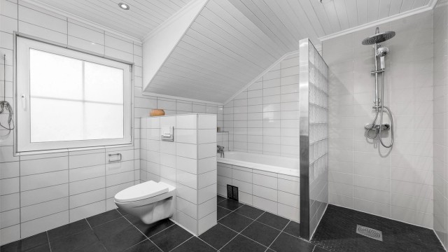 Pent, flislagt bad med varmekabler i gulvet, utstyrt med både dusjhjørne og badekar.