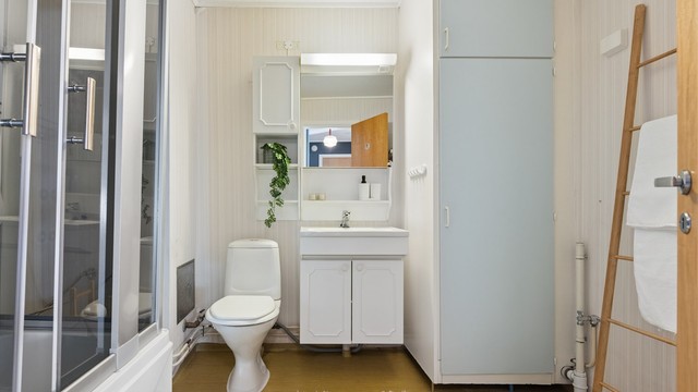 Badet har gulvbelegg, tapetserte vegger og malt himling. Innredningen består av servant med speil og skap, dusjkabinett/badekar og gulvstående toalett.