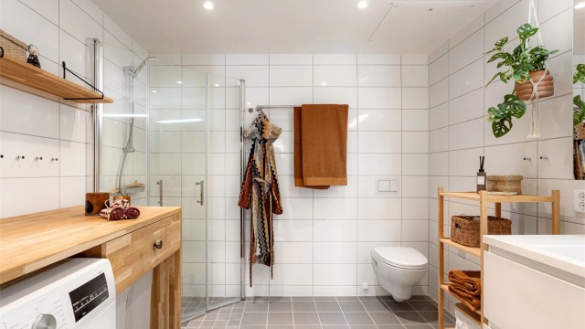 Et moderne og romslig bad med flislagte overflater, opplegg for vaskemaskin og gode oppbevaringsløsninger.
