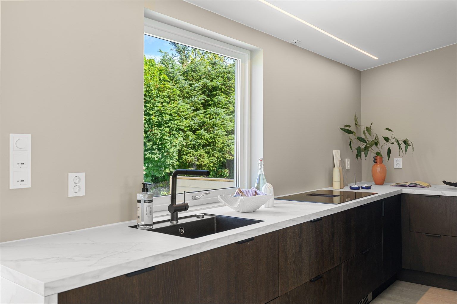 Moderne Epoq-kjøkken fra 2025. Kjøkkenet har mørke fronter og detaljer som spiller godt med boligens ellers lyse fargevalg. Bemerk ventilator fra Franke med integrert nedtrekk.