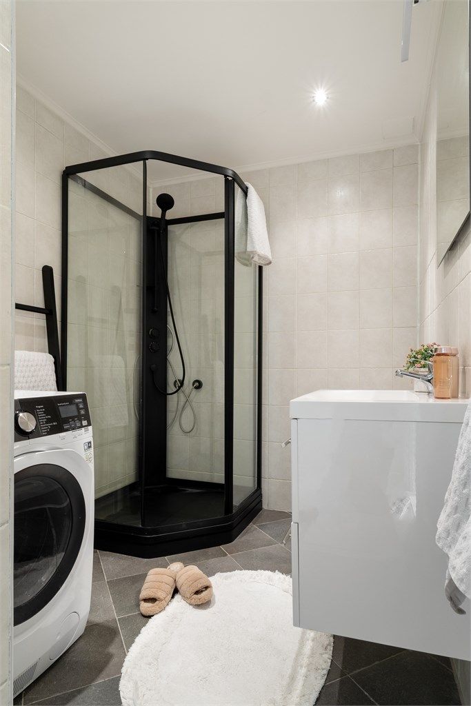Badet har opplegg til vaskemaskin. Dusjkabinett i sorte detaljer.