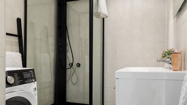 Badet har opplegg til vaskemaskin. Dusjkabinett i sorte detaljer.
