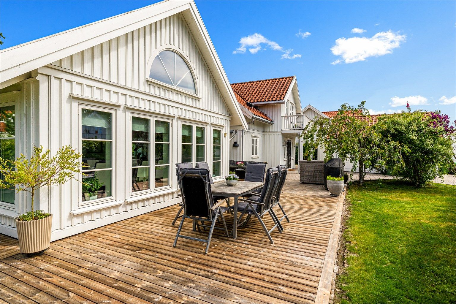 Lettstelt hage med store terrasse flater, gressplen og noe beplanting.
