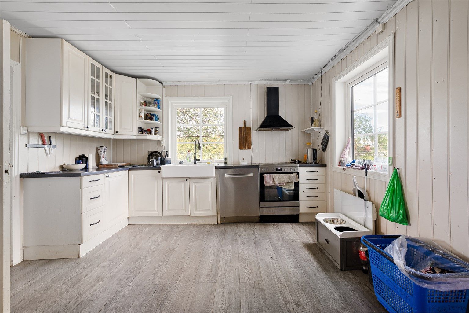 Innredning med profilerte fronter og laminert benkeplate med dobbel keramisk kum. Overskap med belysning, fritthengende ventilator med kullfilter og 3 doble stikkontakter. Hvitevarer som komfyr i nisje, innebygget oppvaskmaskin og kjøl/frys i nisje