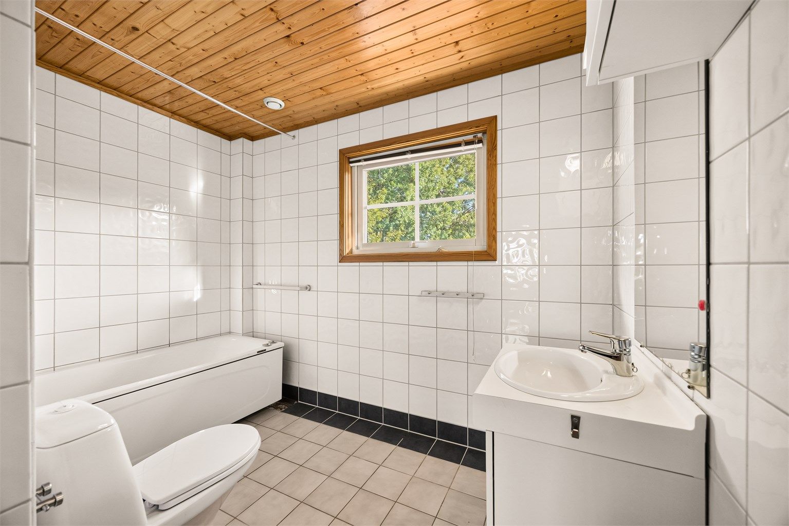 Baderom med flislagte overflater, badekar og rør-i-rør-system. Badet krever oppussing. 