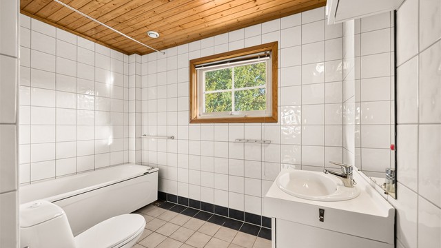 Baderom med flislagte overflater, badekar og rør-i-rør-system. Badet krever oppussing.