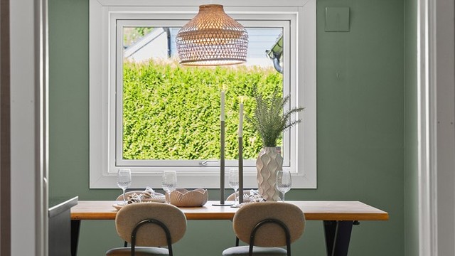 Stort vindu som slipper inn rikelig med naturlig lys, noe som skaper en lys og luftig atmosfære i rommet. Lysinnslippet står i elegant kontrast til kjøkkenets mørke innredning