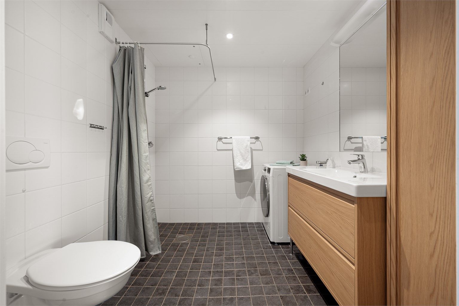 Badet har varmekabler i gulvet og er utstyrt med vegghengt toalett og dusjhjørne.